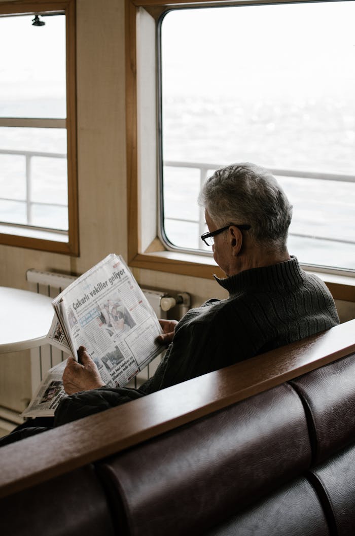 about-us Elderly man reading newspaper inside ferry, enjoying a peaceful travel moment.